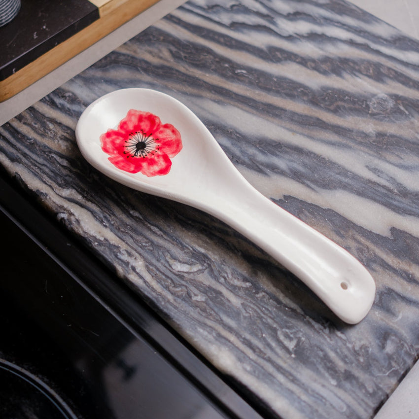 White ceramic spoon rest with floral design on a marble surface