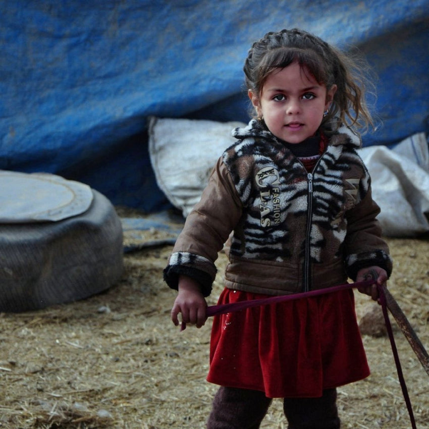 Sweet precious refugee girl in front of a temporary tarp shelter in Iraq